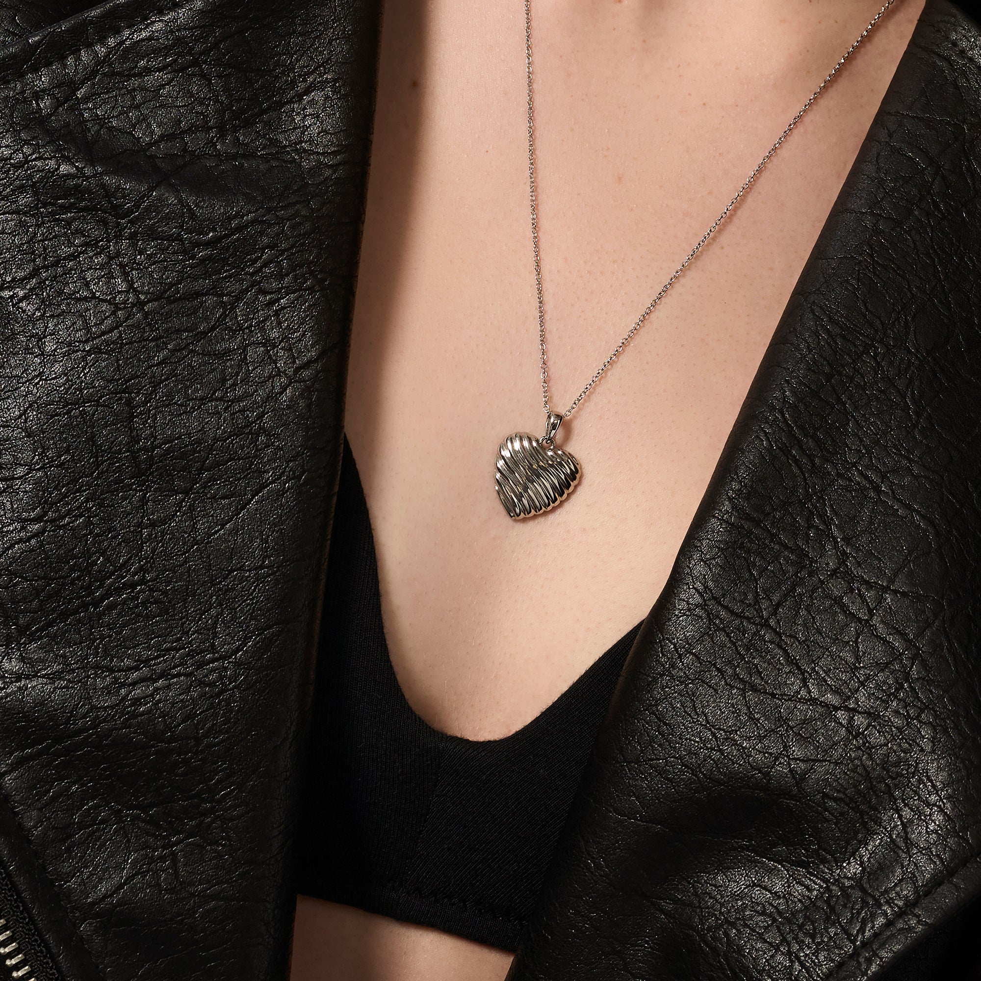 Silver stainless steel ribbed heart pendant necklace worn on neckline, sculptural romantic jewelry, hypoallergenic non-tarnish durable everyday necklace, modern elegant heart jewelry.

